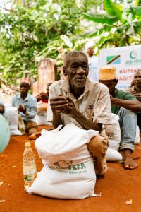 Notre Action An elderly man with a food package during a distribution event in a rural setting.