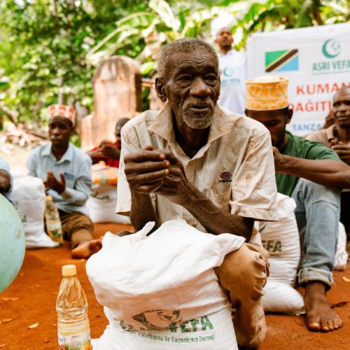 An elderly man with a food package during a distribution event in a rural setting.